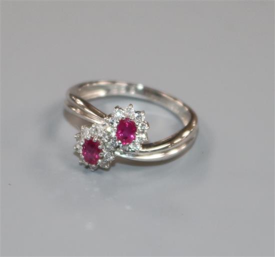 A modern 18ct white gold, ruby and diamond double cluster crossover ring, size M.